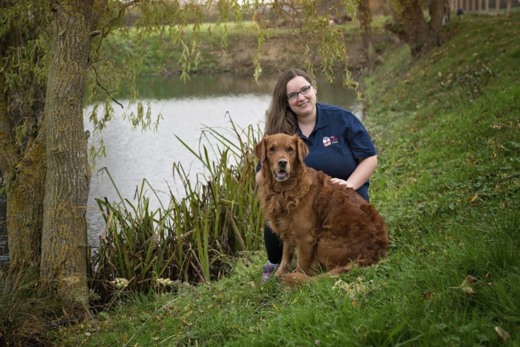 Helen from We Love Pets West Lancs sitting with a dog next to a pond