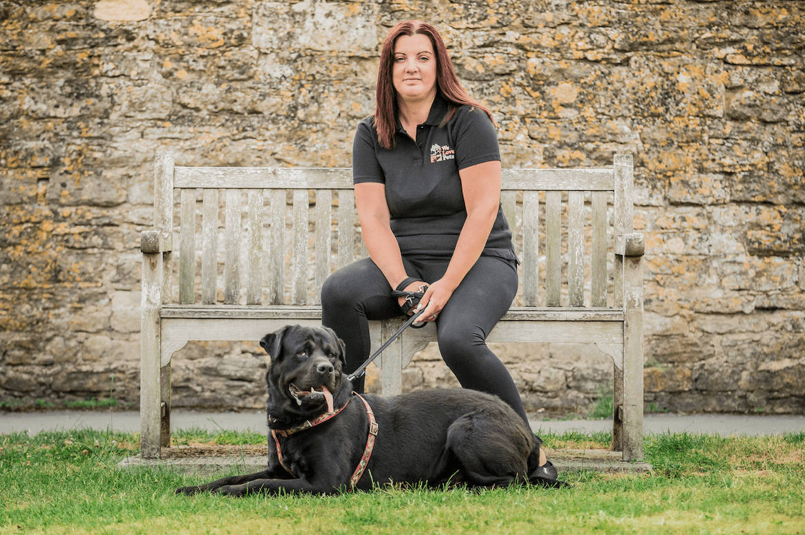 Jo from We Love Pets Dursley sat on a bench with a dog laying down