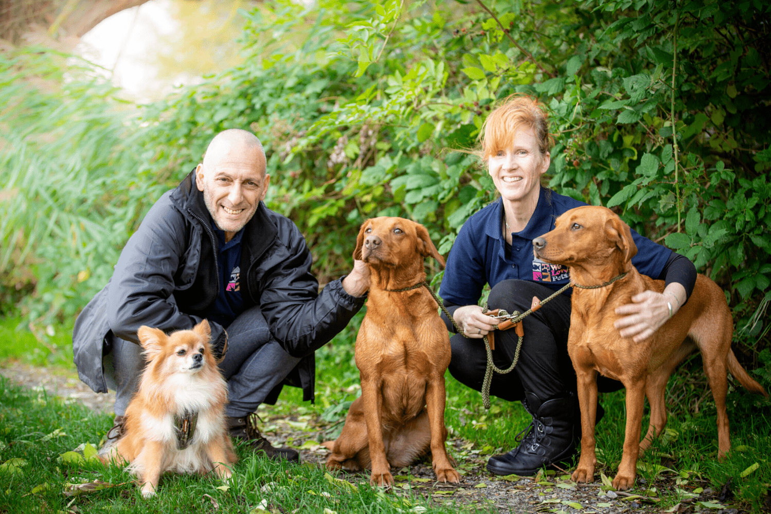 Man and woman from We Love Pets Norwich crouching next to dogs