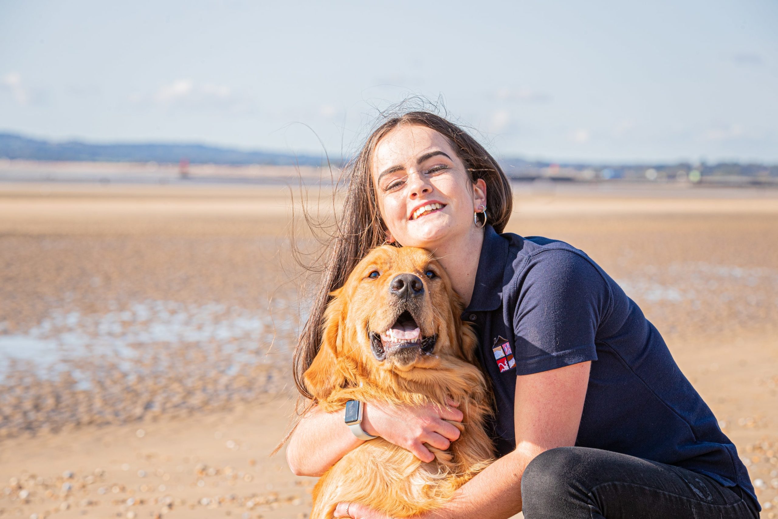 Sophie from We Love Pets Eastbourne hugging dog on a beach